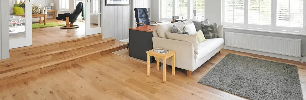 A modern living room with professionally installed laminate flooring, a beige sofa, a small side table, a gray rug, and large windows with white shutters in Madison, WI